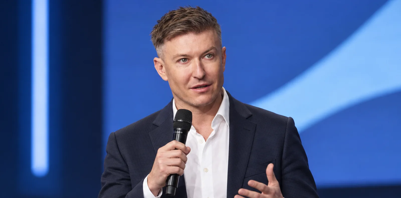 Ilia Zavialov speaking on a conference stage with a handheld microphone